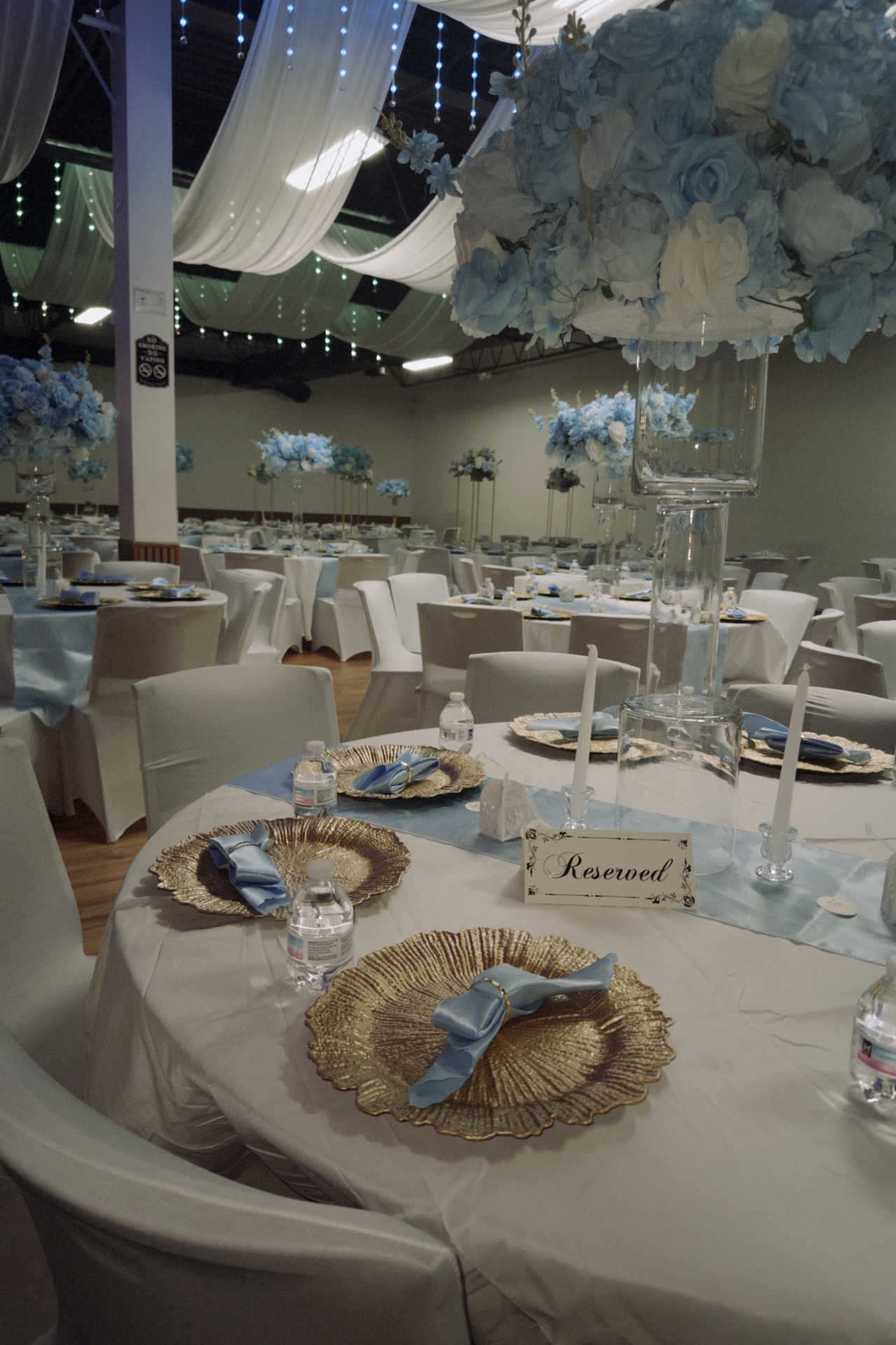 Wedding tablescape with blue runner, gold textured chargers, satin napkins, taper candles, and elevated floral centerpiece.