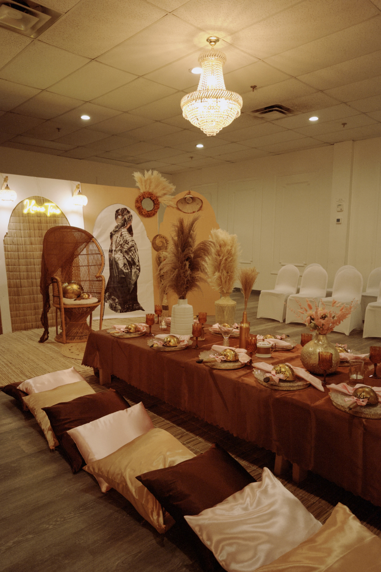 Moody Henne Time room scene with warm chandelier light, long floor table, woven chair, and soft neutral styling.