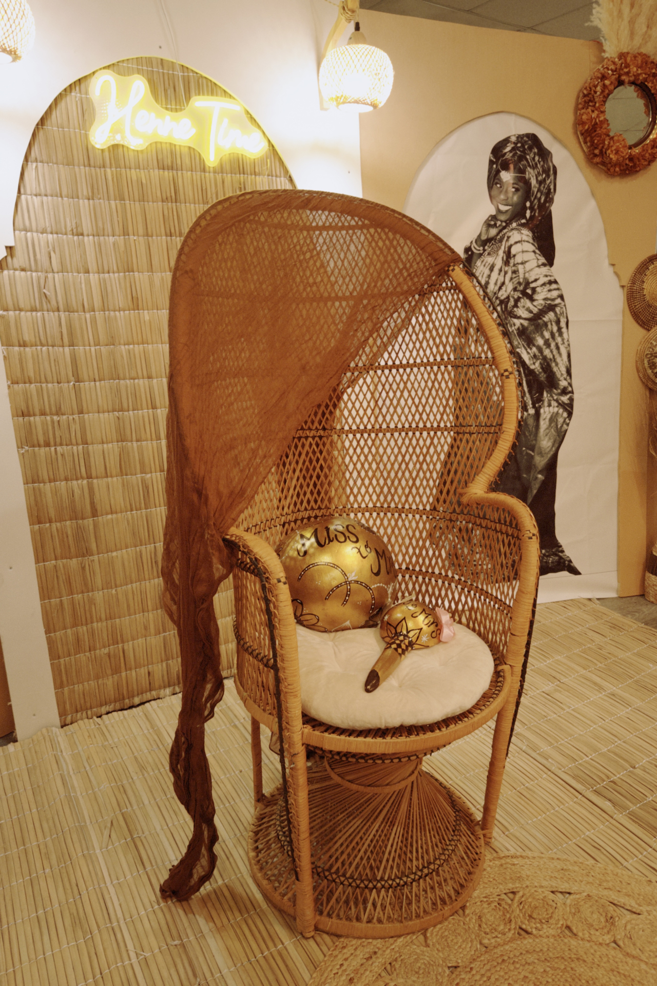 Close view of the Henne Time peacock chair moment with woven textures, gold ceremonial pieces, and neon welcome sign.