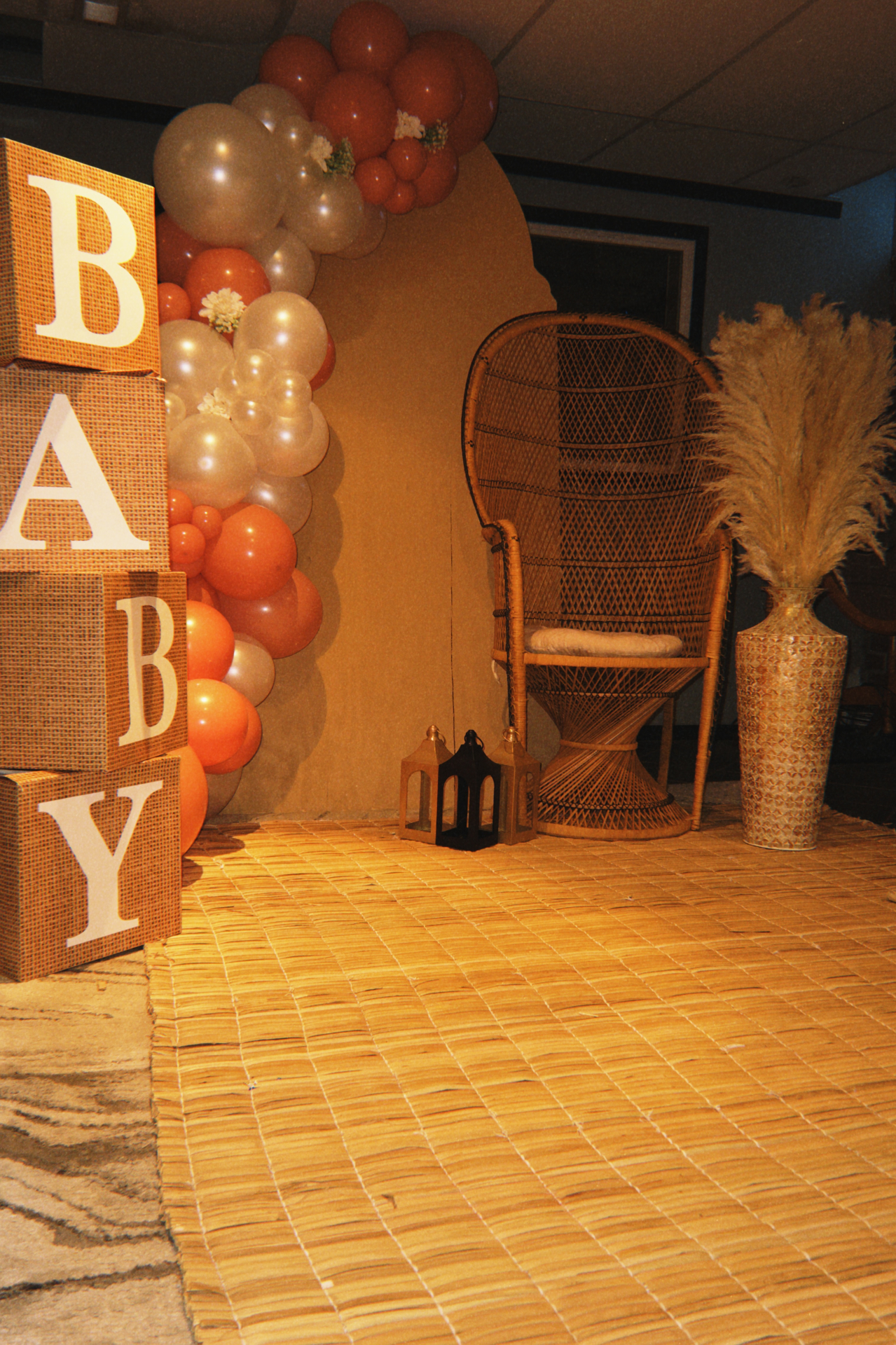 Rouye Time lounge vignette with woven chair, pampas, balloons, and BABY letter blocks.